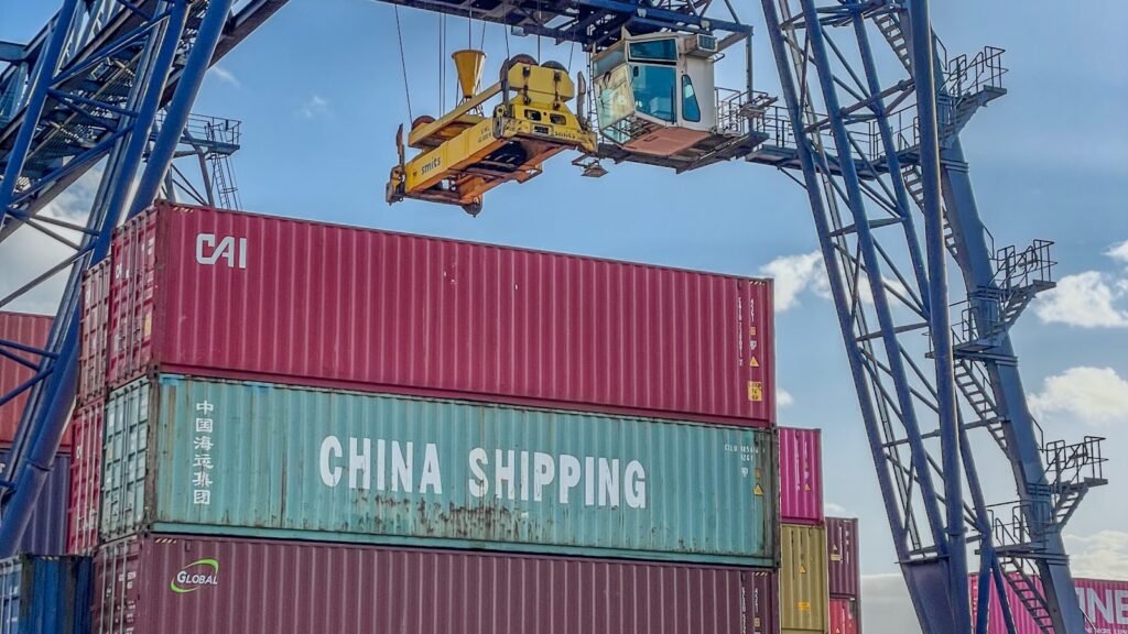 Crane lifting a China Shipping container onto a truck at a busy port