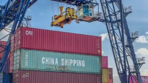 Crane lifting a China Shipping container onto a truck at a busy port